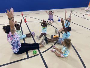 Children and Counselor sitting in a circle with their hands up.