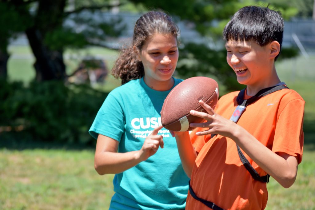 A camper with a football and a staff member watching