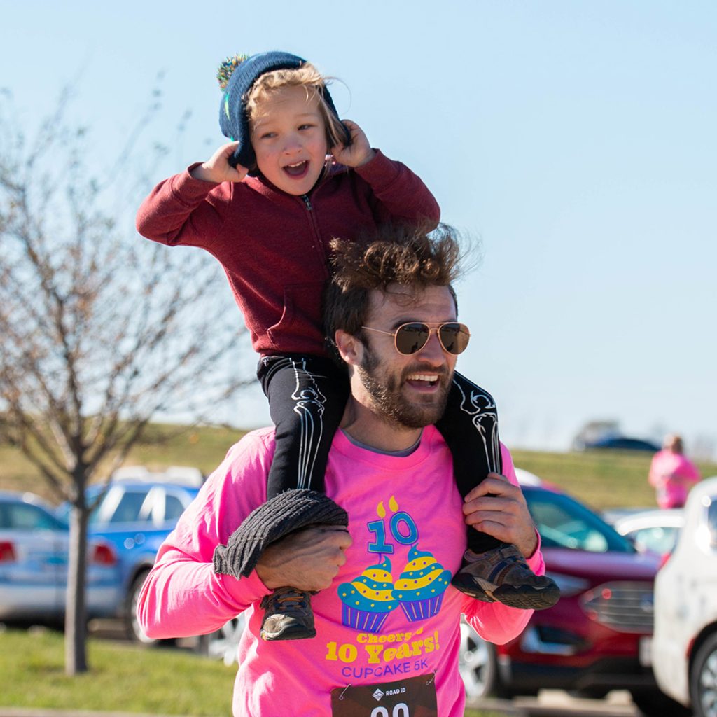 Man running with child on his shoulders while smiling.