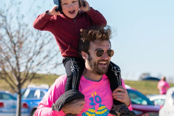 Man running with child on his shoulders while smiling.