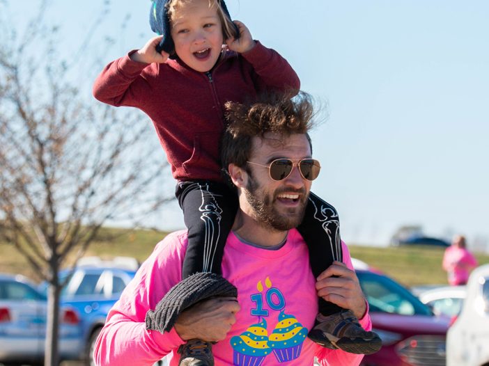 Man running with child on his shoulders while smiling.
