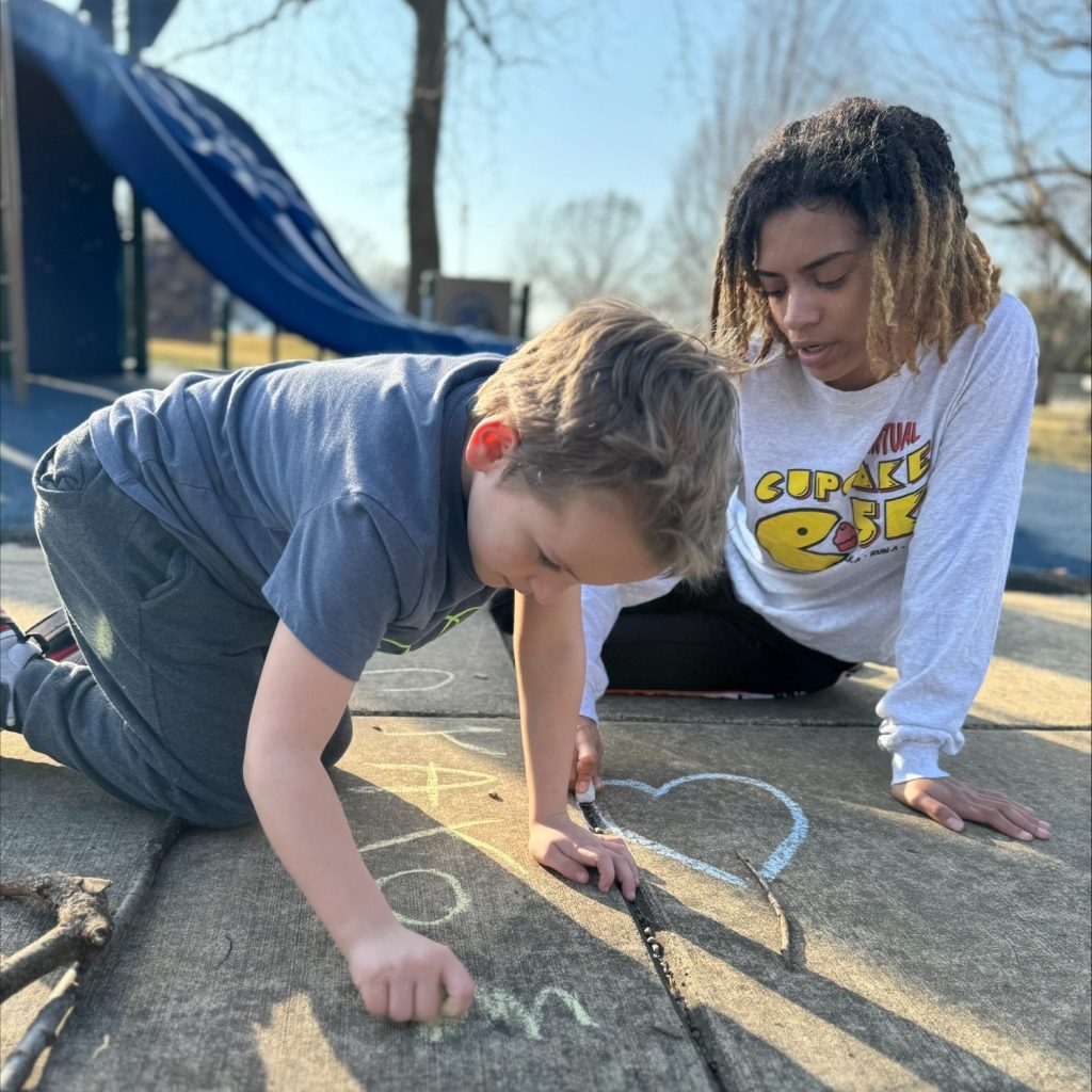 A boy and a young woman drawing with sidewalk chalk