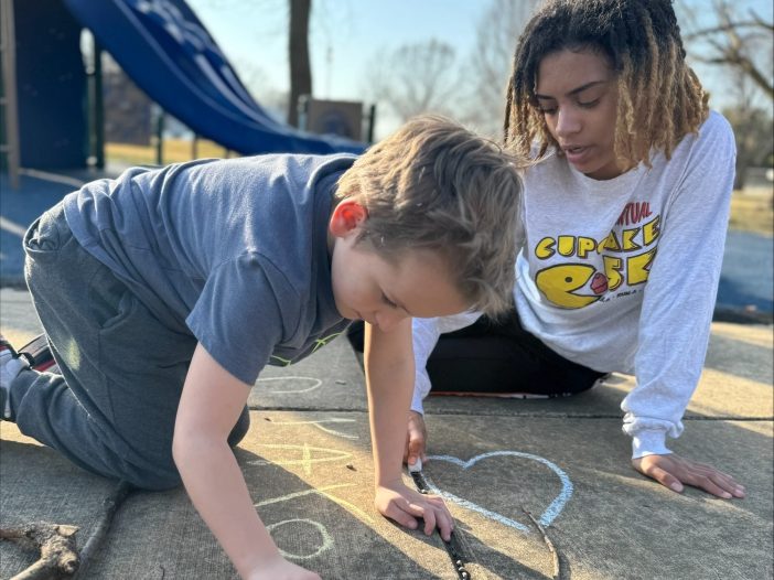 A boy and a young woman drawing with sidewalk chalk