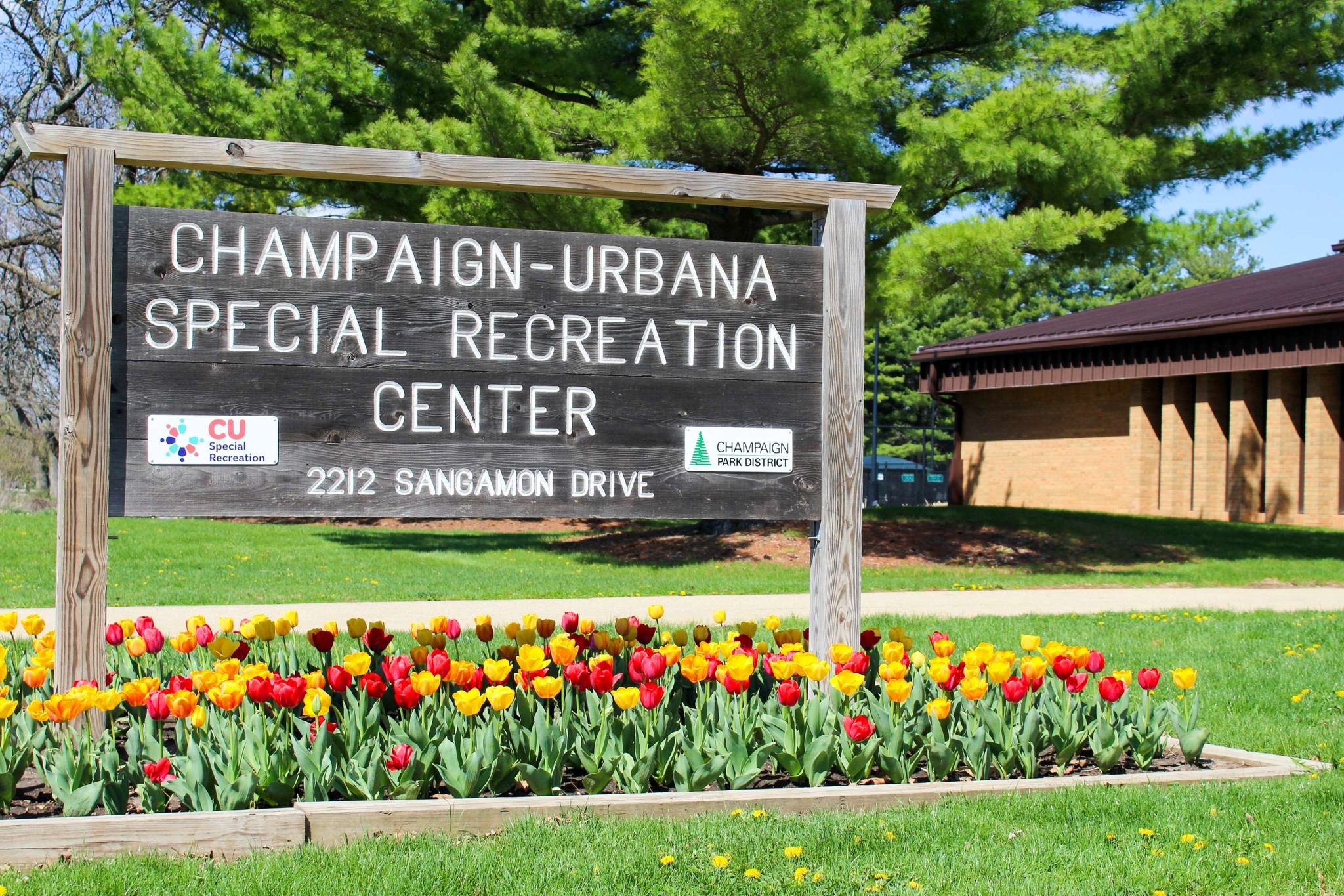 Wooden sign that says Champaign-Urbana Special Recreation Center with red and yellow tulips planted in front